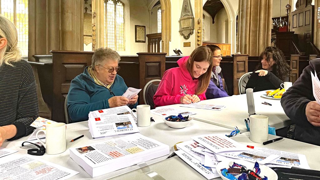 Izzy Foss from Norfolk Community Foundation talks to a older woman whilst taking part in an activity. Rv Annie sits behind talking to another person at the Community Hot Spot in the church.